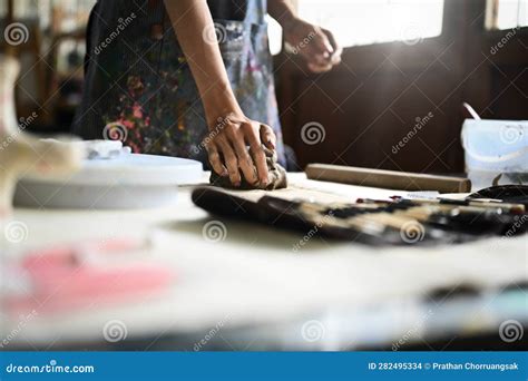 Craftswoman In Apron Kneading Piece Of Raw Clay With His Hands On