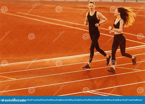 Young Man And Woman Running On Race Track In Modern Stadium Stock