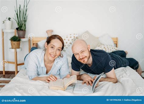 Happy Adult Married Couple In Casual Clothing Reading Books On Bed At