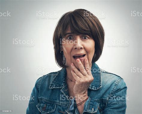 Studio Portrait Of A Senior Woman Looking Shocked Against A Grey