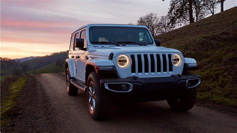 A White Jeep Driving Down A Dirt Road Next To A Hill At Sunset With