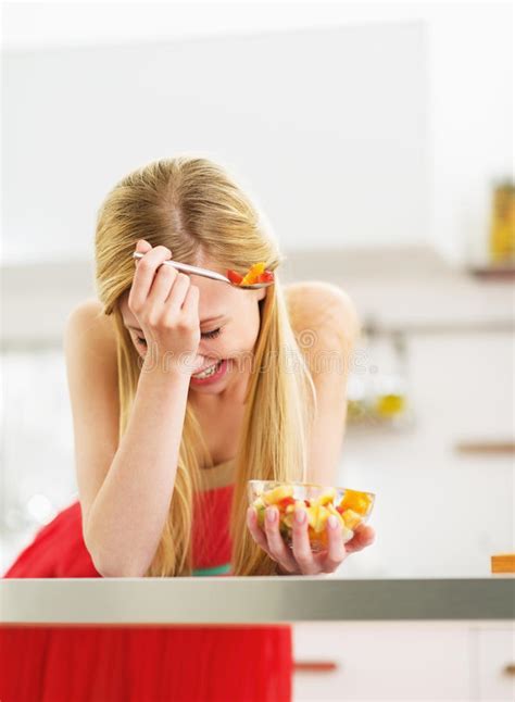 Jovem Mulher De Riso Que Come A Salada De Frutos Frescos Na Cozinha