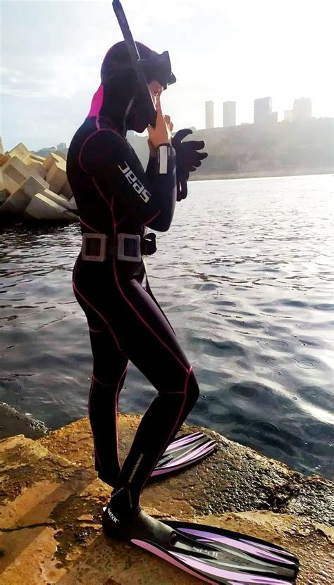 A Man In A Wet Suit Standing On The Edge Of A Cliff Next To Water