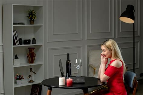 Amour virtuel jolie fille blonde en robe rouge à une date à distance avec du vin et des bougies