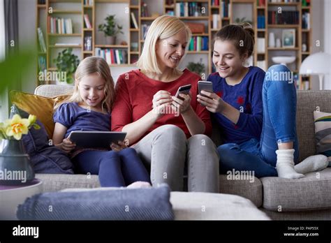 Mother And Her Daughters Sitting On Couch Having Fun Using Digital