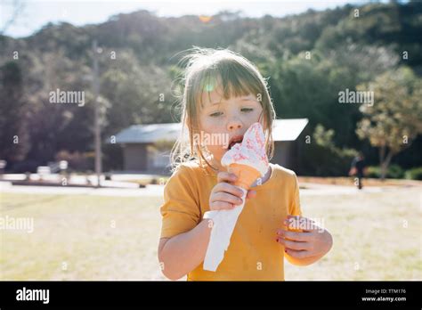 Cute Girl Eating Ice Cream Cone While Standing Against Trees At Park