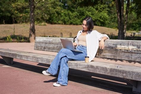 Retrato De Uma Bela Jovem Sentada No Banco Do Parque Usando Laptop E