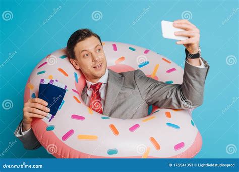 Happy Businessman In Swim Ring Taking Selfie While Holding Passports