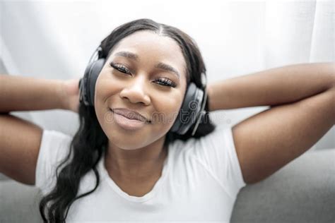 Attractive Young African Woman Sitting On The Couch At Home Listening