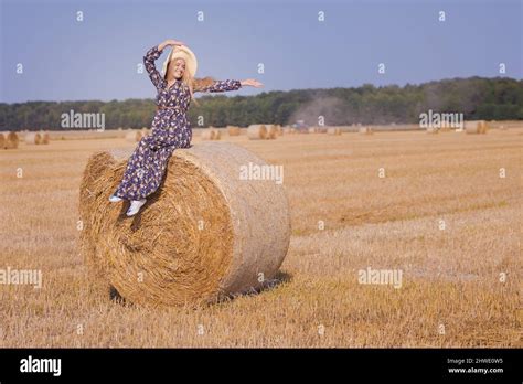 Une jeune fille blonde aux cheveux longs dans un chapeau blanc se repose et pose près des gerbes