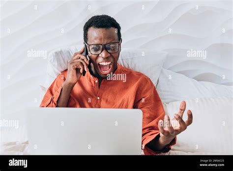 Excited African American Man In Orange Shirt And Glasses Talks On