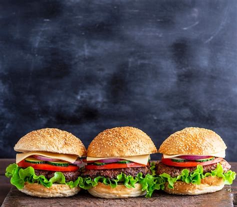 Tres hamburguesas con verduras en una tabla de madera marrón Foto Premium