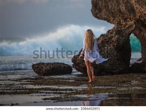 Beautiful Blonde Girl With Long Hair In Short White Dress Running To The Sea At Sunset On The