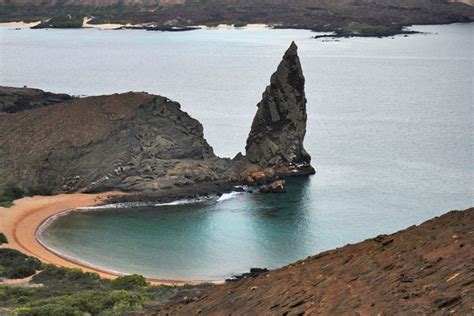 A Large Rock Sticking Out Of The Ocean Next To A Sandy Beach On An Island