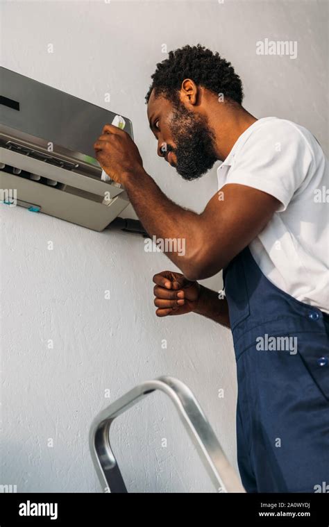 Attentive African American Repairman Standing On Ladder And Fixing Air