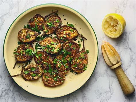 A White Plate Topped With Grilled Eggplant Next To Sliced Lemons And A Wooden Spoon