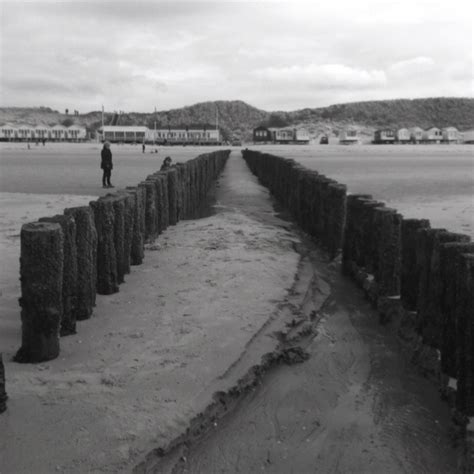 A Man Standing On Top Of A Sandy Beach Next To The Ocean With Wooden Posts