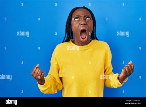 Beautiful Black Woman Standing Over Blue Background Angry And Mad Screaming Frustrated And