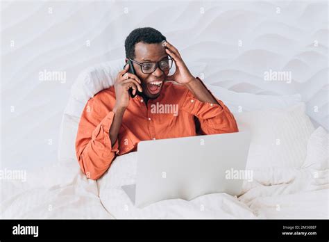 Excited African American Man In Orange Shirt And Glasses Talks On