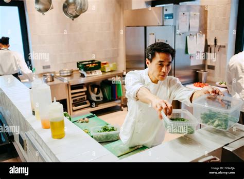 Male chef passing broccolini container while working in commercial ...
