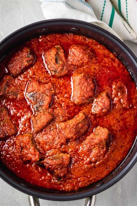 A Pan Filled With Meat And Sauce On Top Of A White Cloth Next To A Fork