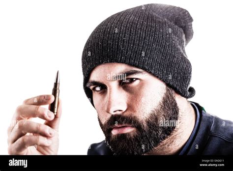 A Bearded Man Wearing A Beanie Hat Holding A Sniper Bullet And Looking