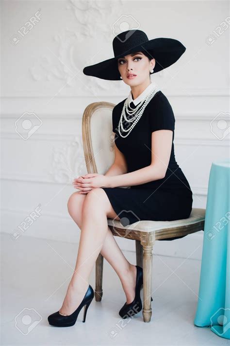 A Woman In A Black Dress And Hat Sitting On A Chair Stock Photo Images