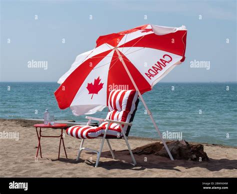 A Canadian Flag Umbrella And Red Stripped Chair On The Beach For Canada