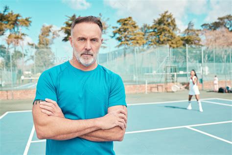 Shot Of A Handsome Mature Coach Standing On A Tennis Court With His Arms Crossed During Practise