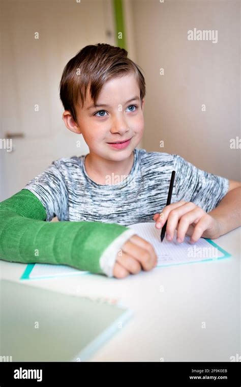 Cool Boy With Green Arm Cast Is Sitting In His Room And Is Writing