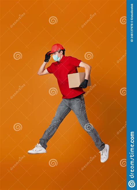 Delivery Man In Face Mask Holding Cardboard Box And Jumping Stock Photo