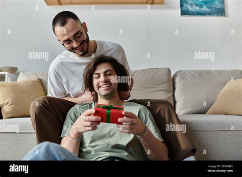 Gay Couple Cuddles On Couch Man Opens Gift Excitedly Stock Photo Alamy