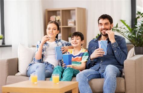 Familia Feliz Con Palomitas Que Ve La Tv En Casa Foto De Archivo