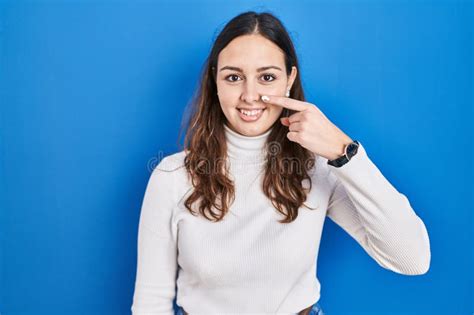 Joven Hispana De Pie Sobre Fondo Azul Señalando Con El Dedo a La Cara