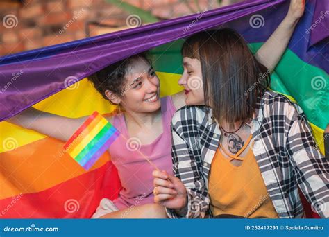 Very Romantic Lesbian Couple On The Sofa Hugging Each Other And Holding The Lgbt Rainbow Flag On