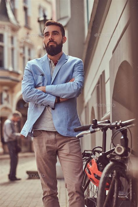 Fashionable Bearded Male Stands With A Bicycle On An Antique Street In