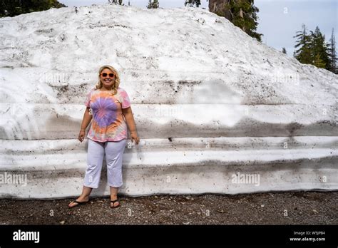 Cute Blonde Tourist Woman Poses And Stands Next To A Large Mound Of Plowed Snow In Lassen