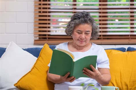 Mulher Idosa Asi Tica Sentada E Lendo Livro No Sof Em Casa Em Relaxar