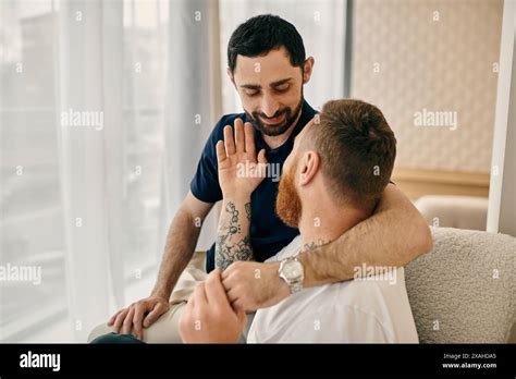 Two Men A Happy Gay Couple Sitting On A Couch In A Modern Living Room Engaged In A Deep And