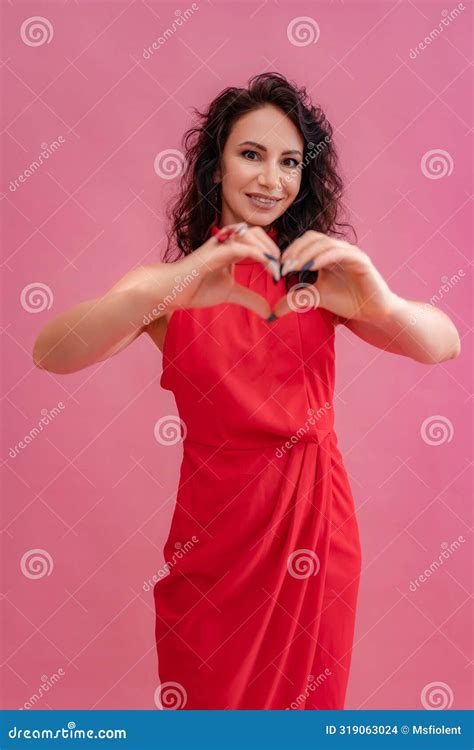 A Woman In A Red Dress Is Smiling And Holding Her Hands Together To Make A Heart Shape Concept