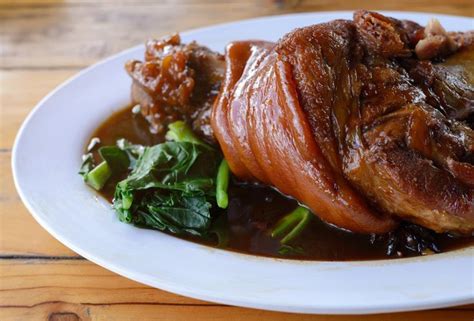 A White Plate Topped With Meat Covered In Gravy Next To Greens And Potatoes