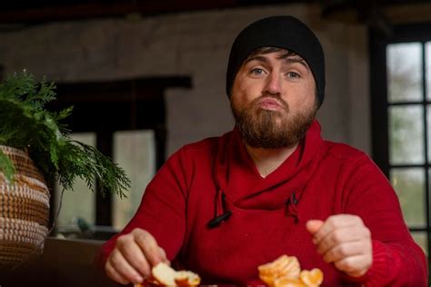 Premium Photo A Man In A Hat And Sweater Eats A Tangerine