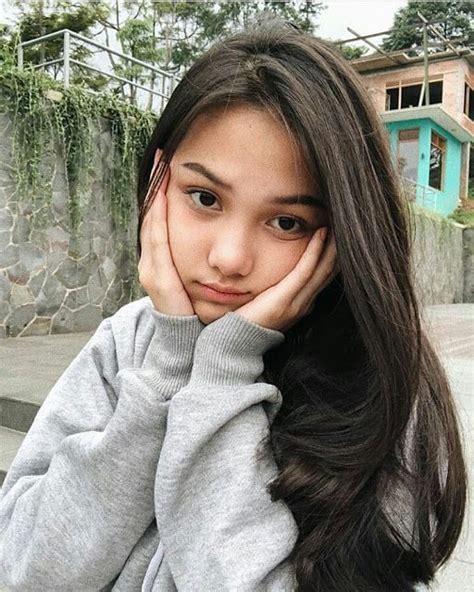 A Girl With Long Brown Hair Is Posing For The Camera While Holding Her Hand To Her Face