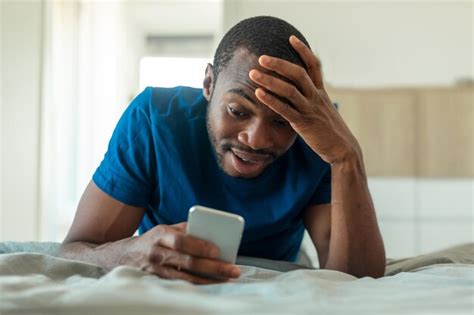 Premium Photo Shocked Black Man Texting On Phone Lying In Bedroom