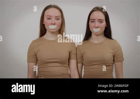 Portrait Of Twin Sisters With Taped Mouth Looking At Camera With Sad