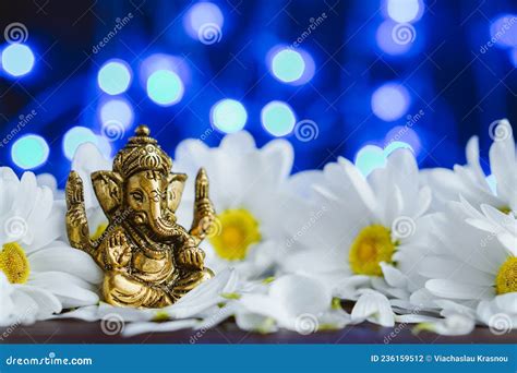 Golden Lord Ganesha Sculpture In Daisy Flowers Over Blue Illuminated