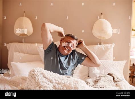 Happy Mature Man Stretching While Sitting On Bed At Home Stock Photo