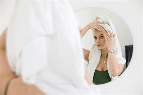 Woman Standing In Front Of A Mirror Applying Cream On Her Face · Free