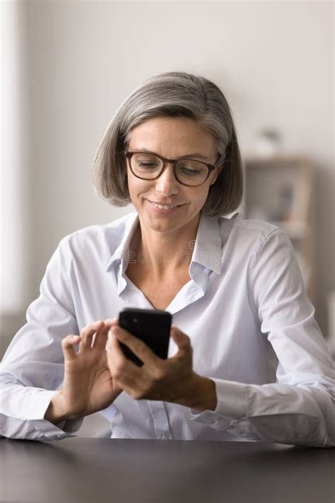 Mature Businesswoman Browsing Market Trends On Her Smartphone In Office