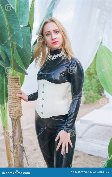 Jeune Fille Blonde Mince D Esclavage Dans La Combinaison Pantalon Noire De Latex Avec Le Corset